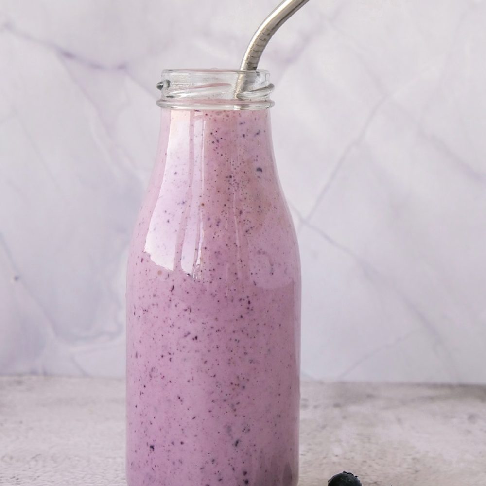 Blueberry smoothie topped with blueberries. A glass of breakfast protein smoothie drink made from pureed raw blueberries, banana, milk, yogurt, and cottage cheese. Vegetarian vegan food